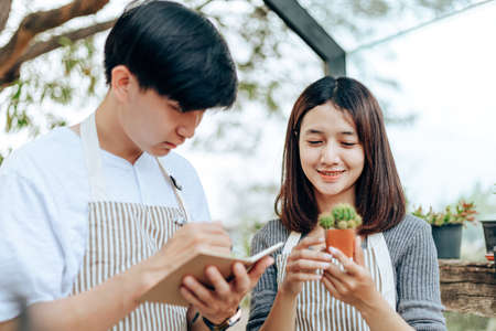 Woman hold cactus and a man writing note in a book. Love couple enjoy hobby with garden cactus.の写真素材