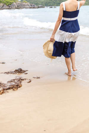 Happy young girl hold hat and walking on the beach. Summer travel, vocation, holiday concept.の写真素材