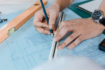 engineers holding a pen pointing to a building and  drawing outlay construction plan as guide for builders with details. Engineer design and writing blueprint.の写真素材
