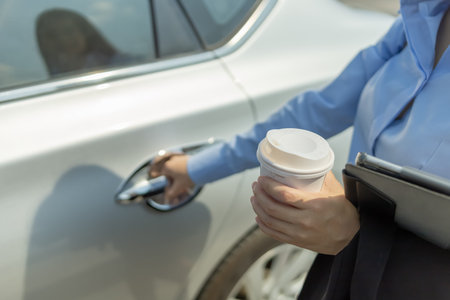 hand of  businesswoman hand hold cup of coffee and tablet and right hand  opening a car door.の写真素材