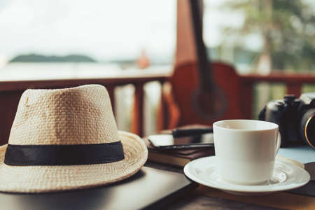 Coffee, straw hat, camera and laptop on the table at resort and beach background.の写真素材