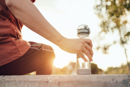 handsome man pick up water bottle on a sunny day after running. Sport, fitness workout concept.