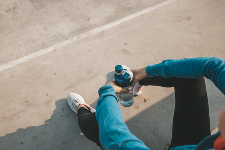 woman athlete thirsty takes a break. she sitting and hold water bottle after running.の写真素材