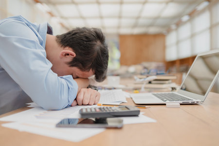 handsome businessman sleepy before working with laptop at desk in office. Working late night and start working early in the morning.の写真素材
