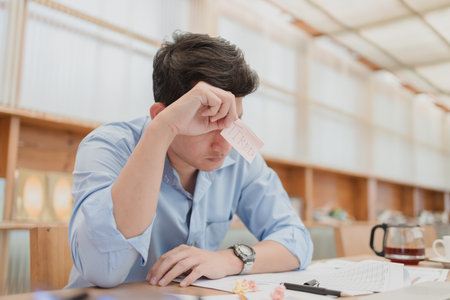 Businessman headache and hold sticky note with text "TIRED". Tired, overworking after long time working with laptop in office.の写真素材