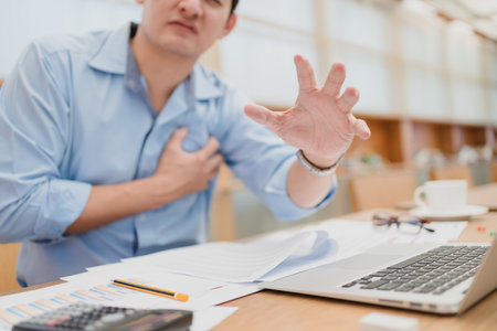 Businessman holding his heart in pain, heart attack, chest pain between working and hands help.の写真素材
