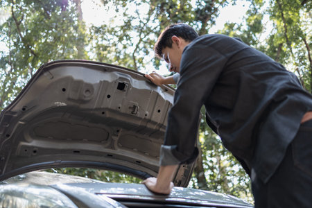 Man' hand open hood of a broken car on the road in the forest. Car breakdown concept.の写真素材