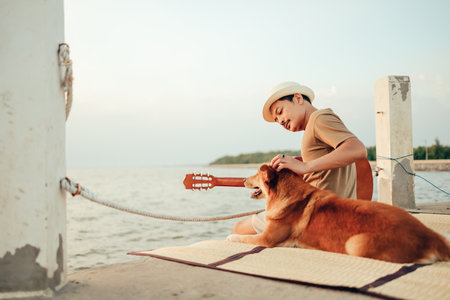 A man wear straw hat and playing guitar music song near the sea sunset and stroking the head dog pet.
Travel, Vocation, Holiday concept.の写真素材
