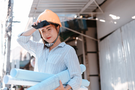Architecture woman hold blueprints design plan and wearing safety helmet at site construction in hot weather day. Architecture, engineering, business and civil concept.の写真素材
