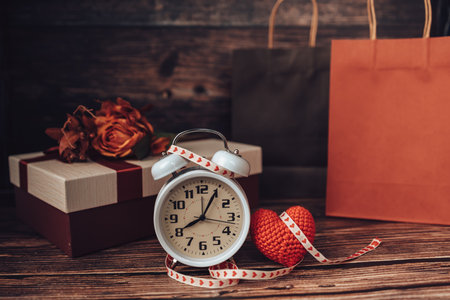 Alarm clock, heart shape and gift box on wood table. Love, gift, valentine concept.の写真素材