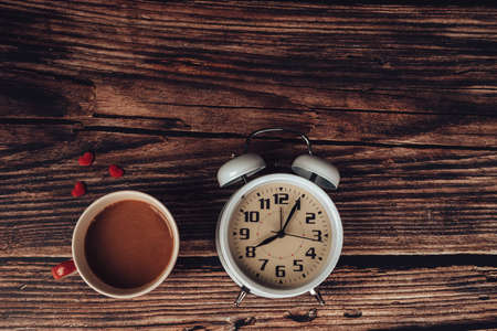 Alarm clock, heart shape and coffee on wood table.の写真素材