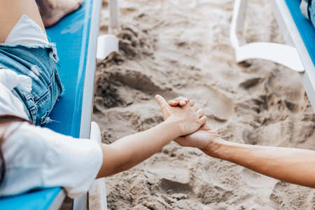 Couple of lovers sitting on beach chair holding hands on the beach in the morning.  Newlywed couple on a romantic vacationの写真素材