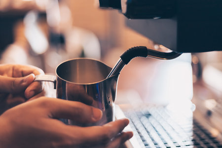 Barista heats milk steam for making lattes at coffee shop.