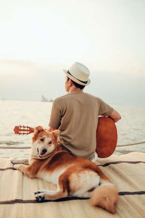 A man wear straw hat and playing guitar music song near the sea sunset with a dog pet.
Travel, Vocation, Holiday concept.の写真素材