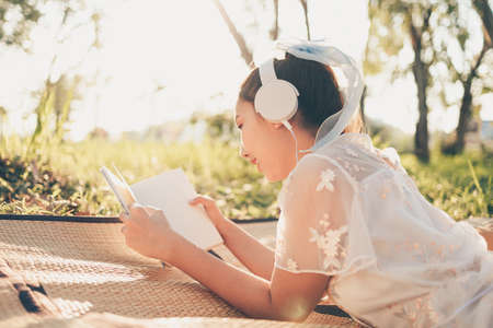A girl in headphone listen music and read novel in the forest. hobby and picnic concept.の写真素材