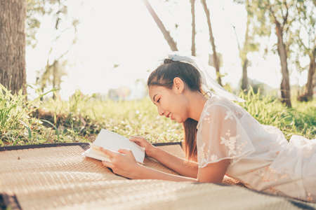 A girl read a novel on straw mat in the forest and light of sunset in the forest. reading hobby and picnic concept.の写真素材