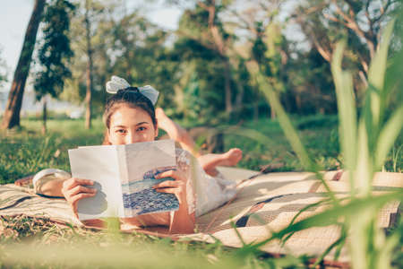 A girl read a novel on straw mat in the forest and light of sunset in the forest. reading hobby and picnic concept.の写真素材