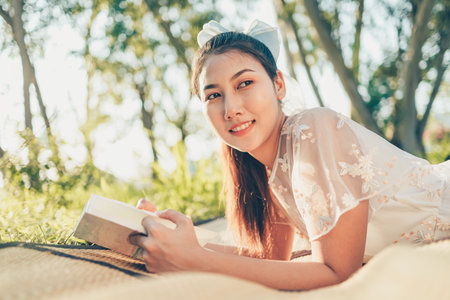 A girl read a novel on straw mat in the forest and light of sunset in the forest. reading hobby and...