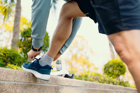 Young man tie running shoes in the park before running. Young man workout before fitness training at the park.の写真素材