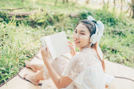 A girl in headphone listen music and read novel in the forest. hobby and picnic concept.の写真素材