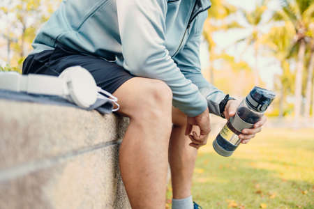 sport man sitting after running and holding water bottle drink. Sport thirsty and resting after exercise.の写真素材