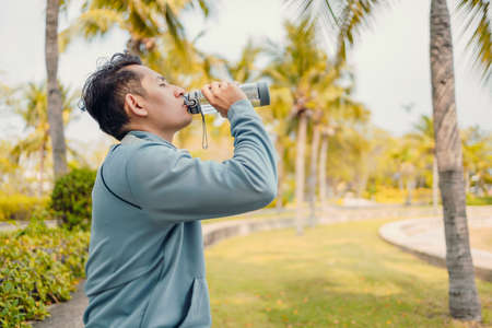 Young sport man drink water after jogging, running in the park. Sport thirsty and resting after exercise.の写真素材