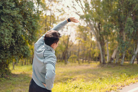 young man stretching in the park before running. Young man workout before fitness training at the park. Healthy and exercise young man warming up on the road beside the forest.の写真素材