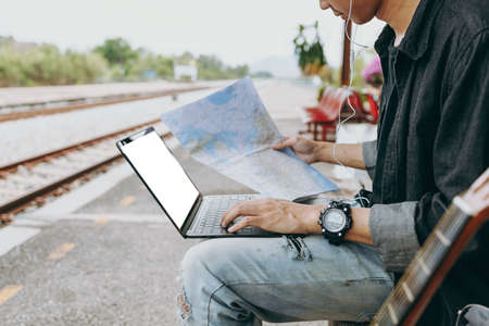 Young asian man using laptop and check map for working and search location for travel at train station. Freelance work and travel concept.の写真素材