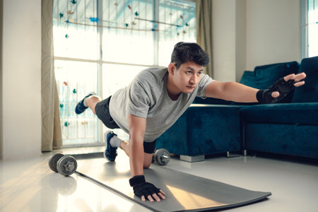 Young man making abdominal exercises on yoga mat in living room at home. Fitness, workout and...