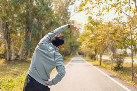 young man stretching in the park before running. Young man workout before fitness training at the park. Healthy and exercise young man warming up on the road beside the forest.の写真素材
