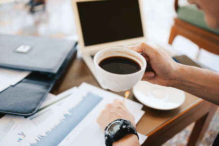 businessman holding coffee cup in hands and computer on table in coffee shop. Young freelancer drink coffee and working.の写真素材