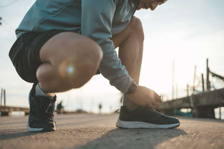 closeup of man tying shoe laces on the road before running in sunset. Sport and workout concept.の写真素材