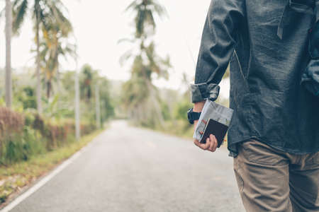 rear view of man with backpack hold passport and map hiking and walking on the road in forest. Backpack travel concept.の写真素材