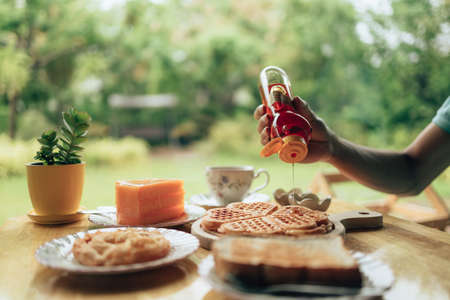 Hand pouring honey on fresh waffles on wood plate. Waffle and dessert concept.の写真素材