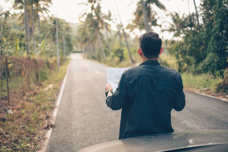 A man with backpack hiking read a map in front of car on the road in forest. Backpack travel concept.の写真素材