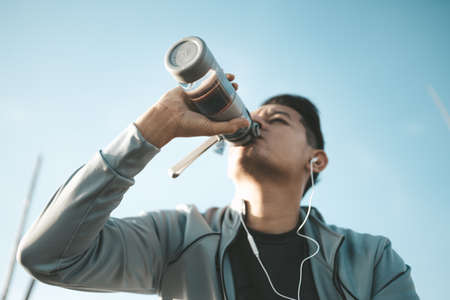 Young sport man drink water after jogging, running in the park. Sport thirsty and resting after exercise.の写真素材