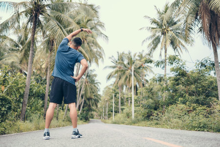 young man stretching in the park before running. Young man workout before fitness training at the park. Healthy and exercise young man warming up on the road in the forest.の写真素材