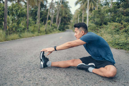 young man stretching in the park before running. Young man workout before fitness training at the park. Healthy and exercise young man warming up on the road in the forest.の写真素材