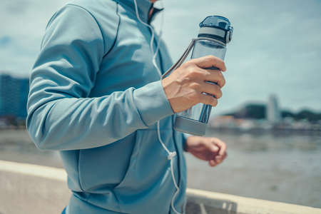 Young sport man hold water bottle and listen music while jogging and running on the road  in the park and city background.の写真素材