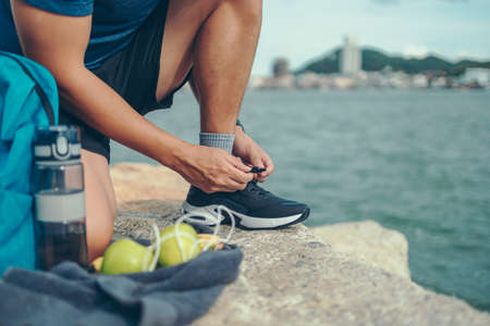 closeup of man tying shoe laces on the stone before running near the beach and city background. Sport and workout concept.の写真素材