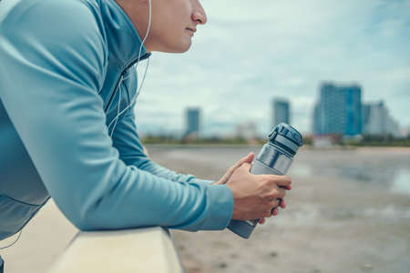 sport man standing after running and holding water bottle drink. Sport thirsty and resting after exercise.の写真素材