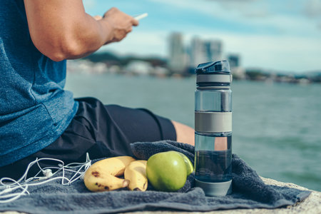 Water bottle, banana, earphone, green apple and towel on the ground beside young man rest after...