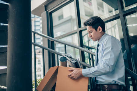 Unemployed hold cardboard box and laptop bag, dossier and drawing tube in box. Quitting a job, businessman fired or leave a job concept.の写真素材