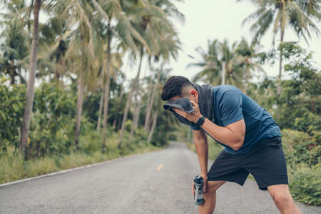 sport man resting after a running and wipe the sweat by towel and hand hold water bottle. sport and workout concept.の写真素材