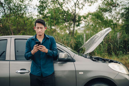 young man calling,  texting for car service on roadside assistance after broken car. Car broken, car breakdown concept.の写真素材