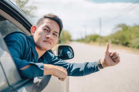 hand giving a thumbs up sign throw the window of a car broken on the road. Symbol of a hand for...
