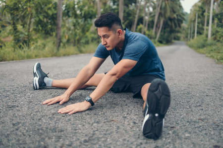 young man stretching in the park before running. Young man workout before fitness training at the park. Healthy and exercise young man warming up on the road in the forest.の写真素材