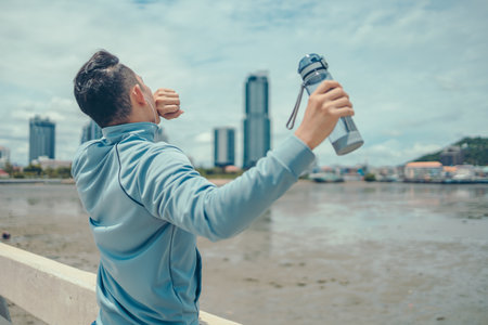 The young athlete stood yawning and twisting lazily and holding a water bottle in his right hand the morning before his workout.の写真素材