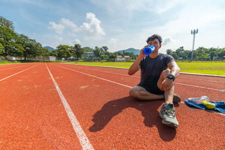 Young man stretching muscles before and after training and drink water from water bottle. Fitness and sport concept.の写真素材