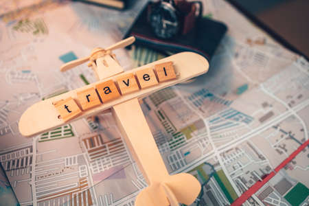 Wood square with word "travel" on airplan model, watch, money wallet, passport, camera on road map. Object for travel concept.の写真素材